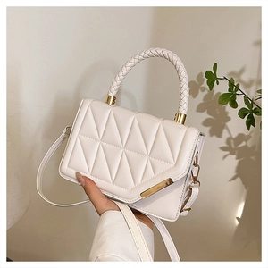 Detail of white quilted crossbody bag with woven handle and gold hardware accents