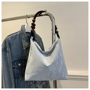 Detail of silver pleated tote bag with dark brown wooden bead handle on hanger