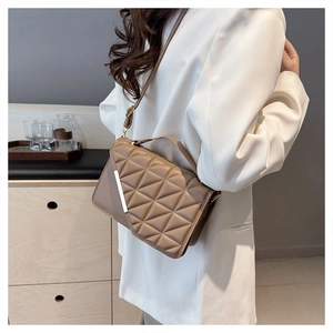 Detail of khaki quilted crossbody bag with gold metal trim worn by model in white blazer