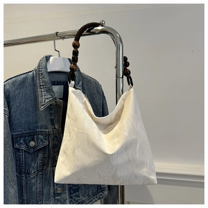 Close-up of white hobo bag with unique dark wooden bead shoulder strap detail