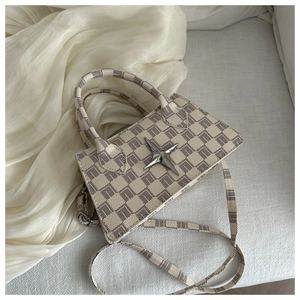 Macro view of checkered pattern handbag with star-shaped metal emblem and shoulder strap
