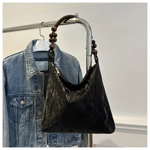 Detailed close-up of a black pleated tote bag featuring a retro wooden bead shoulder strap