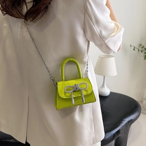 Mini sac bandoulière vert fluo avec nœud en strass porté par un mannequin en blanc