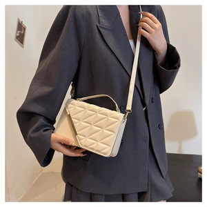 Close-up of cream quilted crossbody bag with geometric stitching on gray blazer