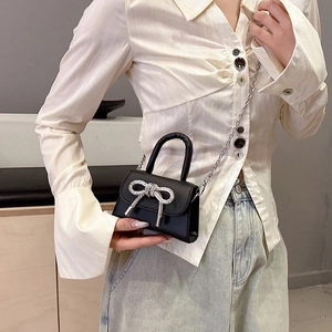 Mini sac à main en cuir noir avec nœud en strass et chaîne porté par un mannequin