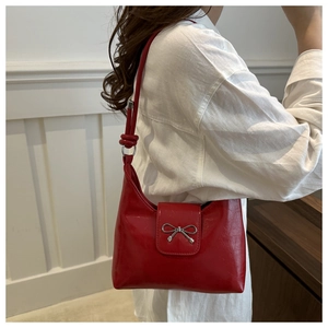 Detail of red glossy shoulder bag with silver bow buckle worn by a model in white shirt