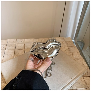 Macro detail of a silver lip-shaped evening clutch bag with glossy mirror finish and chain