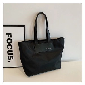 Detail of minimalist black nylon tote bag showing durable texture and FASHION patch