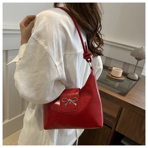 Red patent leather underarm bag with silver bow detail shown on model in cozy cafe setting
