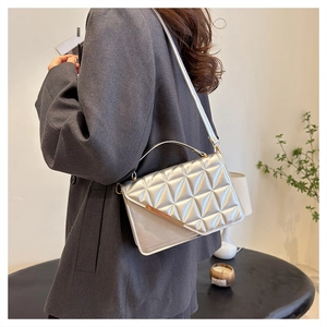 Detail shot of a silver quilted handbag styled on a model in a gray suit blazer