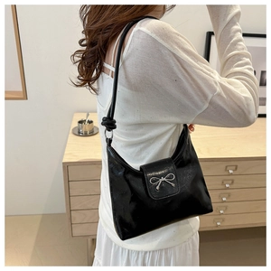 Detail of glossy black moon bag with silver bow buckle worn over the shoulder