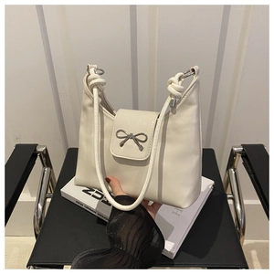 Detail of cream-colored shoulder bag with bow metal buckle and knotted rope handle design