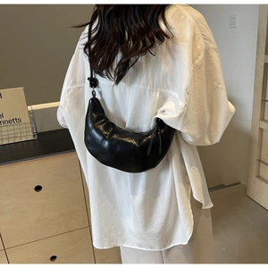 Detail of minimalist black crescent bag with glossy leather finish and knot strap