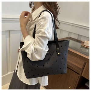 Detail of grey star-print tote bag with black strap and golden rivets worn by model