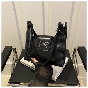 Detailed shot of a black glossy leather shoulder bag featuring a silver bow metal clasp