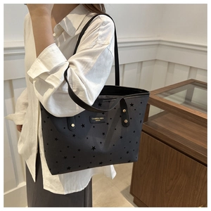 Detail of black tote bag with star patterns and logo plate on a shoulder strap