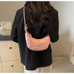 Detail of pink croissant bag with knotted strap worn by model in black blazer