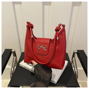 Detail of red patent leather handbag with silver metal bow and knotted strap design