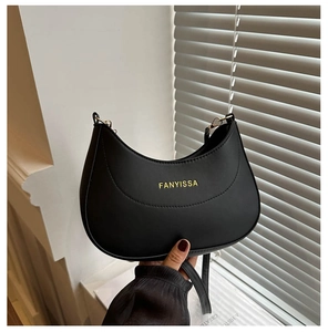 Détail d'un sac demi-lune noir avec logo doré sur un fond minimaliste blanc moderne