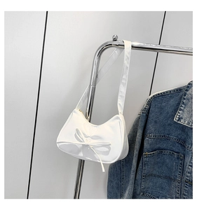 Nahaufnahme einer weißen Halbmond-Schultertasche mit eleganter Schleife am Kleiderbügel
