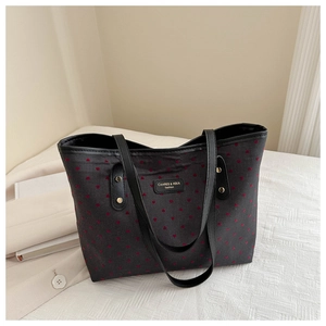 Detail of the black tote bag with red heart print, leather handles, and gold rivets