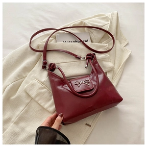 Close-up of glossy burgundy tote bag featuring a metallic bow buckle and smooth leather texture