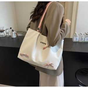 Detail of white tote bag with pink bow accents and metal heart charms worn on shoulder