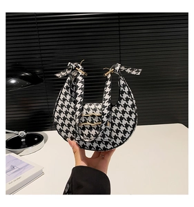 Detail of crescent houndstooth handbag with wavy golden hardware and matching strap