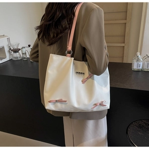 Close-up of white tote bag featuring pink ribbons and silver heart charms in a cafe setting