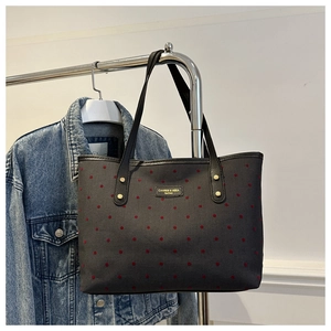 Detail of black tote bag with red polka dots and metal brand logo hanging with denim jacket