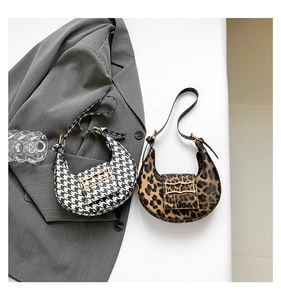 Flat lay of leopard print and houndstooth crescent shoulder bags with gold wavy buckles