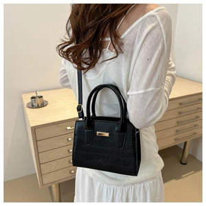 Détail d'un sac bandoulière noir motif pierre avec boucles dorées porté par un modèle