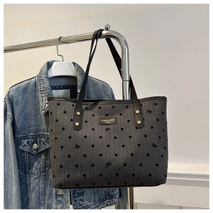 Detail of grey denim tote bag featuring black star patterns and leather shoulder strap