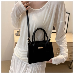 Sac à bandoulière en similicuir noir tendance avec fermoir doré sur une tenue blanche