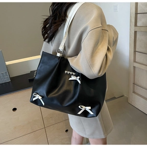 Detail of black tote bag with white bows and heart studs shown on shoulder