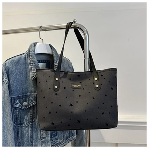 Detail of star print tote bag with metal logo plate and gold rivets on black shoulder strap