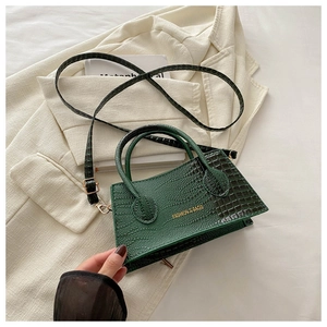 Close-up of crocodile embossed texture and golden lettering on dark green handbag