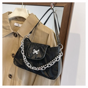 Detail of black patent leather baguette bag with silver butterfly and chain accents