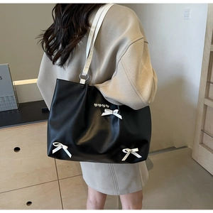 Detail of black tote bag with white bows, heart rivets, and leather texture for women