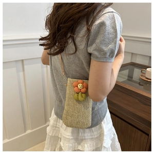 Detail of mini straw crossbody bag with plush orange smiley flower and thin strap