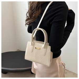 Détail du sac à main beige gaufré crocodile avec finitions dorées porté par un modèle