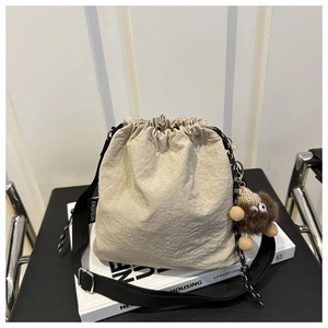 Dettaglio della borsa a secchiello beige con coulisse e ciondolo in peluche