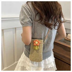Detail of woven straw crossbody phone bag featuring a plush flower and brown leather strap