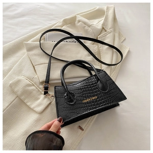 Detail of black crocodile texture handbag with gold lettering on a beige blazer background