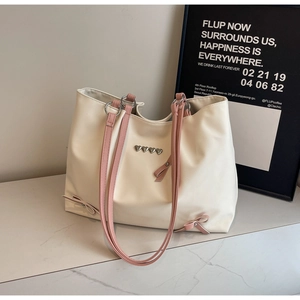 Detail of cream tote bag with pink straps, heart studs, and decorative side bows