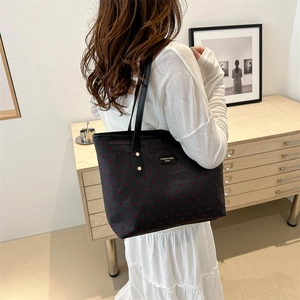 Black tote bag with red heart pattern and metal logo plate worn by a model in a studio