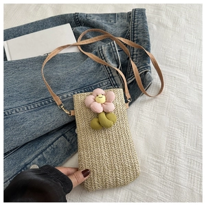 Detail of woven straw mini crossbody bag with colorful plush flower accents and slim strap