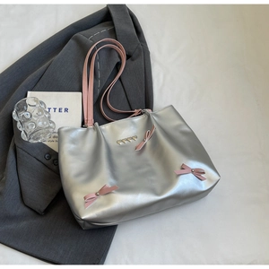 Detailed shot of silver tote bag with pink bows and heart accents on a grey blazer