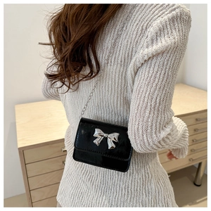 Détail du petit sac noir brillant avec nœud argenté porté sur un pull en maille blanc