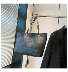 Detail of black leather tote bag with geometric stitching and gold chain strap